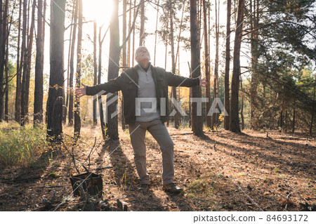Senior hiker outstretched arms while enjoying sunrise at the forest among the trees Senior hiker outstretched arms while enjoying sunrise at the forest among the trees 84693172