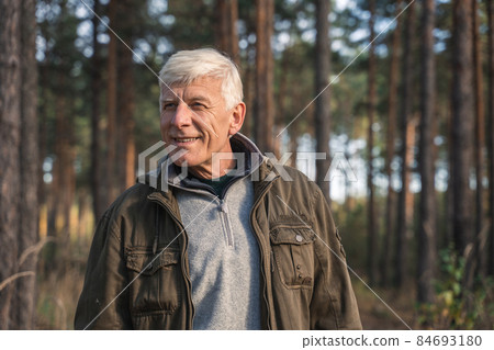 Mature male person standing at the forest around the trees and smiling toothy Mature male person standing at the forest around the trees and smiling toothy 84693180