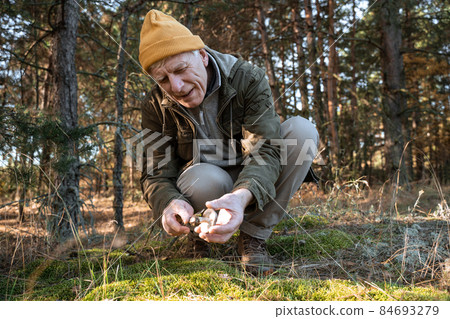 Old man sitting with mushroom on the ground in the forest Old man sitting with mushroom on the ground in the forest 84693279