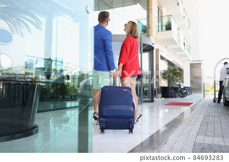 Couple dressed in luxury suits come to hotel with suitcase Couple dressed in luxury suits come to hotel with suitcase 84693283
