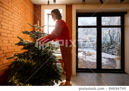 Woman decorating Christmas tree at home Woman decorating Christmas tree at home 84694740