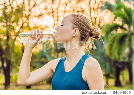 Attractive sporty woman drinking water from a bottle after jogging or running Attractive sporty woman drinking water from a bottle after jogging or running 84694969