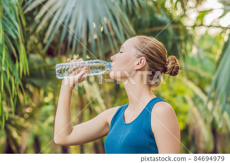 Attractive sporty woman drinking water from a bottle after jogging or running Attractive sporty woman drinking water from a bottle after jogging or running 84694979