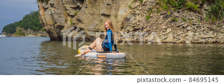 BANNER, LONG FORMAT Young women Having Fun Stand Up Paddling in the sea. SUP. Red hair girl Training on Paddle Board near the rocks 84695145