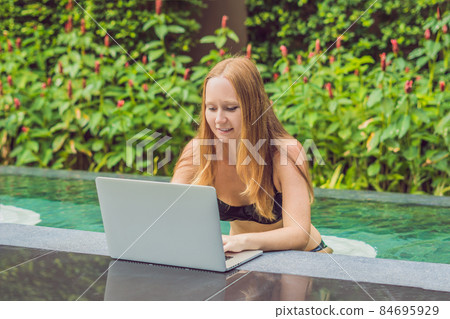 Young female freelancer sitting near the pool with her laptop in the hotel browsing in her smartphone. Busy at holidays. Distant work concept. Copy space for your text Young female freelancer sitting near the pool with her laptop in the hotel browsing in her smartphone. Busy at holidays. Distant work concept. Copy space for your text 84695929