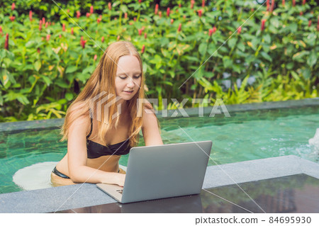 Young female freelancer sitting near the pool with her laptop in the hotel browsing in her smartphone. Busy at holidays. Distant work concept. Copy space for your text Young female freelancer sitting near the pool with her laptop in the hotel browsing in her smartphone. Busy at holidays. Distant work concept. Copy space for your text 84695930