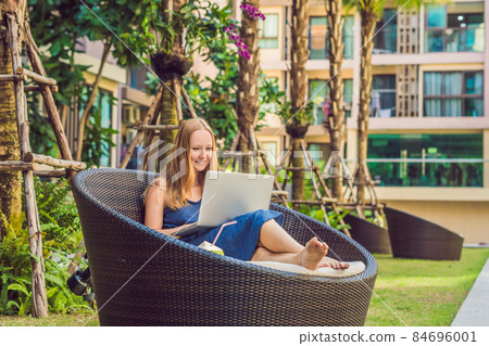 Young female freelancer sitting near the pool with her laptop in the hotel browsing in her smartphone. Busy at holidays. Distant work concept. Copy space for your text 84696001