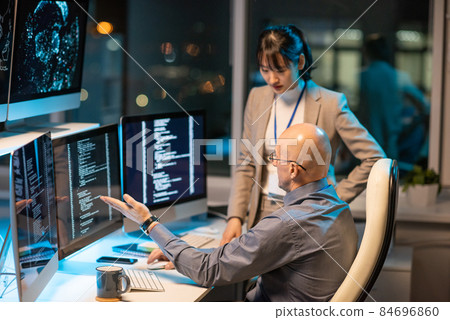 Two intercultural colleagues interacting in front of computer monitors Two intercultural colleagues interacting in front of computer monitors 84696860