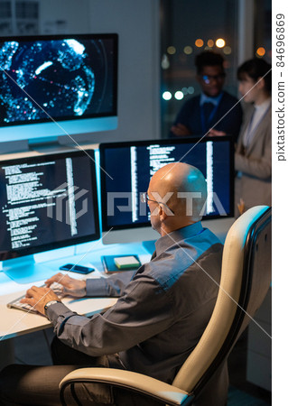 Bald mature businessman decoding data on computer screen Bald mature businessman decoding data on computer screen 84696869
