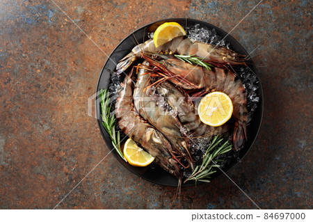 Fresh tiger prawns in a black plate with lemon, rosemary and crushed ice. 84697000