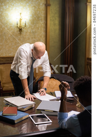 Bald mature lawyer bending over table while reading document 84697238