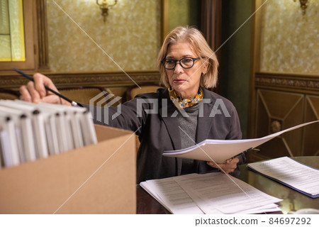 Mature blond lawyer revising juridical documents in folders Mature blond lawyer revising juridical documents in folders 84697292