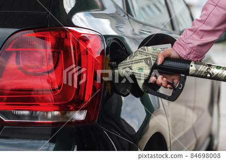 Woman's hand fuels the car. Girl at the gas station fills the tank with gasoline fuel. The rise in fuel prices, a concept idea. Filling gun and money dollar 84698008