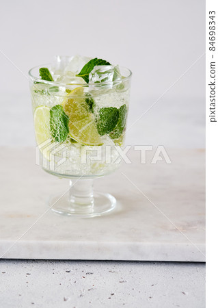 Cold refreshing summer lemonade mojito in a glass on a grey concrete or stone background. Copy space. Cold refreshing summer lemonade mojito in a glass on a grey concrete or stone background. Copy space. 84698343
