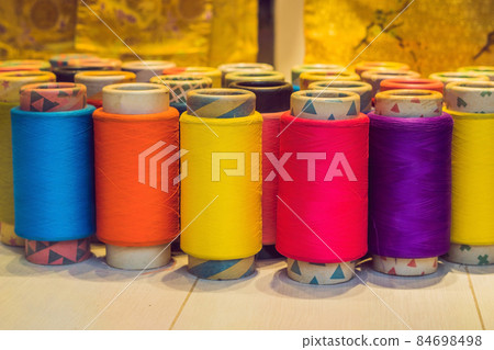 Background with a lot of colorful coils with threads. Bobbins are stacked in three rows, one on the other. The winding is erratic. Multicolored threads 84698498