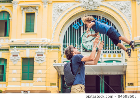 Father and son on background Saigon Central Post Office in Ho Chi Minh, Vietnam. On the building there is an inscription in Vietnamese: a post office Father and son on background Saigon Central Post Office in Ho Chi Minh, Vietnam. On the building there is an inscription in Vietnamese: a post office 84698603