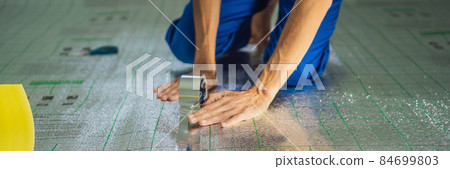BANNER, LONG FORMAT Master installs the overlapping thermal insulation in the room. Floor heating installation. Male hand holds reinforced tape. Repair in the apartment, floor insulation BANNER, LONG FORMAT Master installs the overlapping thermal insulation in the room. Floor heating installation. Male hand holds reinforced tape. Repair in the apartment, floor insulation 84699803