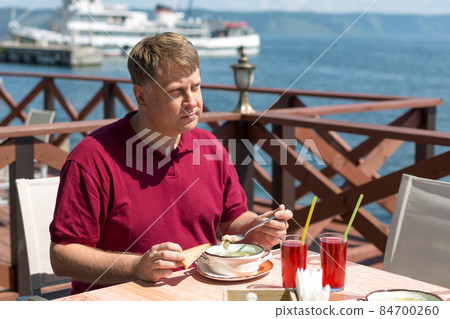 An adult blonde man has lunch on the beach in a cafe in the fresh air An adult blonde man has lunch on the beach in a cafe in the fresh air 84700260