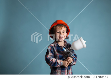 Cute little caucasian child wearing hard hat holding electric spray gun Cute little caucasian child wearing hard hat holding electric spray gun 84700537