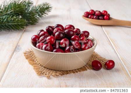 Ripe red cranberries in a beige bowl over white rustic wooden table. 84701363