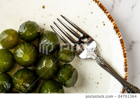 Top view of preserved whole green figs and dessert fork on a white porcelain plate. Top view of preserved whole green figs and dessert fork on a white porcelain plate. 84701364