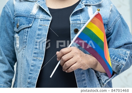Asian lady wearing blue jean jacket or denim shirt and holding rainbow color flag, symbol of LGBT pride month celebrate annual in June social of gay, lesbian, bisexual, transgender, human rights. Asian lady wearing blue jean jacket or denim shirt and holding rainbow color flag, symbol of LGBT pride month celebrate annual in June social of gay, lesbian, bisexual, transgender, human rights. 84701468