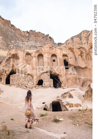 Happy young woman on background of ancient cave formations in Cappadocia, Turkey. The Monastery is one of the largest religious buildings. Happy young woman on background of ancient cave formations in Cappadocia, Turkey. The Monastery is one of the largest religious buildings. 84702306