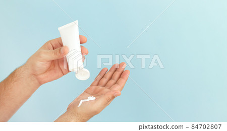 Man apply cosmetic skin care moisturizer cream on blue background Man apply cosmetic skin care moisturizer cream on blue background 84702807