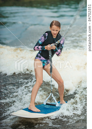 Active beautiful girl in the swimsuit standing on the wakeboard in the river 84702851