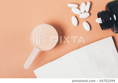 Whey protein powder in measuring spoon next to amino acid pills Whey protein powder in measuring spoon next to amino acid pills 84702894