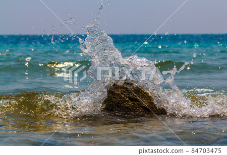 Waves hitting round rocks and splashing Waves hitting round rocks and splashing 84703475