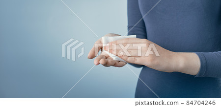 Young woman cleaning her hands by using white antibacterial napkin on gray background. Photo with copy space. Young woman cleaning her hands by using white antibacterial napkin on gray background. Photo with copy space. 84704246