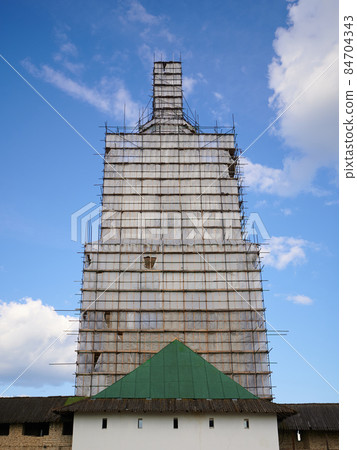 Scaffolding from planks around old bell tower. Background blue sky with clouds. 84704343