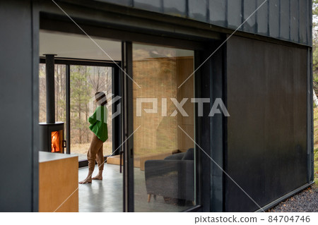 Young woman stands near fireplace at modern house on nature Young woman stands near fireplace at modern house on nature 84704746