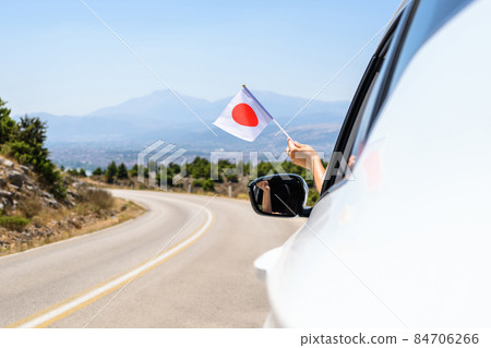 Woman holding Japan flag from the open car window driving along the serpentine road in the mountains. Concept 84706266