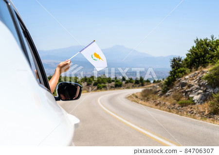 Woman holding Cyprus flag from the open car window driving along the serpentine road in the mountains. Concept Woman holding Cyprus flag from the open car window driving along the serpentine road in the mountains. Concept 84706307