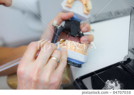 Technician dental is working with complete lower and upper metal ceramic prosthesis dental. Dental technician works by brush with jaw model 84707038