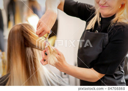 Cutting female blonde hair. Hairdresser cuts hair of a young caucasian woman in a beauty salon close up. Cutting female blonde hair. Hairdresser cuts hair of a young caucasian woman in a beauty salon close up. 84708868