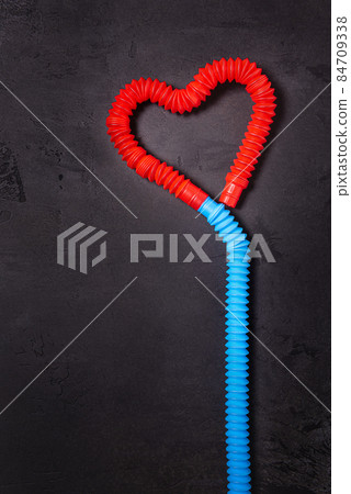 Tube toys bent as red heart balloon and blue ribbon on black concrete Tube toys bent as red heart balloon and blue ribbon on black concrete 84709338