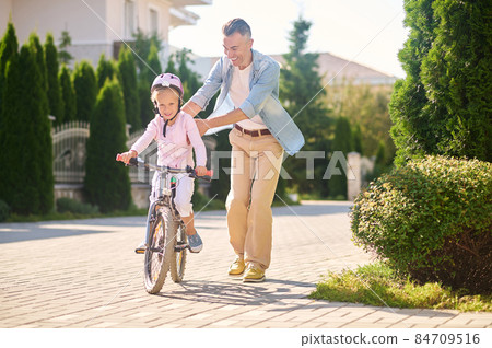 Dad helping his daughter learn riding a bike 84709516