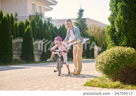 Dad helping his daughter learn riding a bike Dad helping his daughter learn riding a bike 84709517