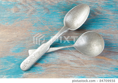 Two old metal spoons on blue wooden background. 84709938