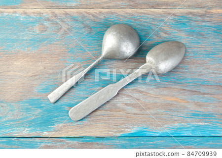 Two old metal spoons on blue wooden background. 84709939