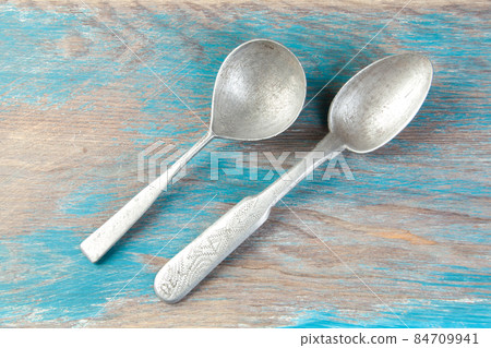 Two old metal spoons on blue wooden background. 84709941