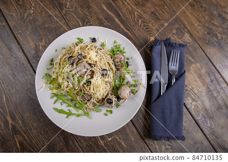 Spaghetti with meatballs, olives and arugula on wood table 84710135