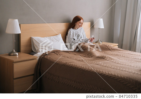 Attractive relaxed young woman enjoy shopping online with credit card and mobile phone lying in bed at home. 84710335