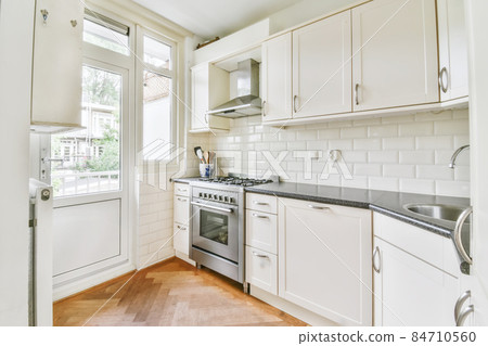 Interior of spacious light kitchen with modern white furniture in light apartment Interior of spacious light kitchen with modern white furniture in light apartment 84710560