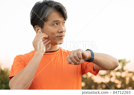Upper body of a middle-aged man preparing for jogging with his smartwatch in his arms in the evening 84712265