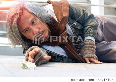 A homeless man is sitting on walkway in town. He is seeing sky and hoping to have the better life. poverty, despair, Photo Sympathetic and hope concept. A homeless man is sitting on walkway in town. He is seeing sky and hoping to have the better life. poverty, despair, Photo Sympathetic and hope concept. 84716192