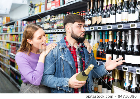Young family couple deciding what sparkling wine to buy in grocery store 84716386